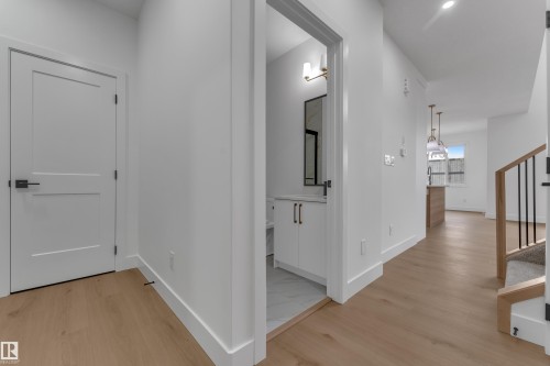 Light wood-finish flooring, white flat panel door with black hardware, white walls, built-in vanity with white cabinetry, and a wood and metal staircase - 178 Munn Way, Leduc, AB 