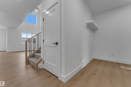 Wood-finish flooring throughout, white interior doors with contemporary black hardware, staircase with carpeted treads and metal spindles, built-in wall paneling detail, and high ceilings with upper-level windows - 178 Munn Way, Leduc, AB 
