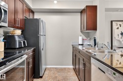Kitchen featuring dark wood-finish cabinetry, stainless steel appliances, dark stone-finish countertops, a double basin sink, and tile flooring - 