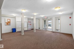 Spacious common area featuring textured carpet flooring, multiple ceiling-mounted light fixtures, and a glass-paneled entrance door - 