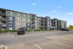 Multi-story building featuring a facade with mixed siding and stone accents, individual balconies, and an expansive paved parking lot - 