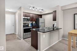 Kitchen featuring wood cabinetry, stainless steel appliances, a double basin sink, and a dark stone countertop with a breakfast bar - 