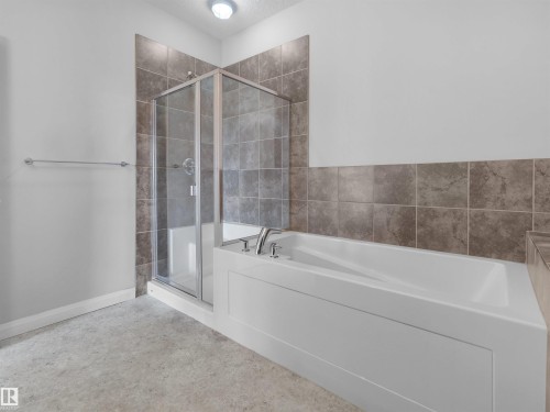 Tiled shower enclosure with clear glass doors, adjacent soaking tub with chrome fixtures, and a tiled accent wall - #415 2588 Anderson Wy Sw, Edmonton, AB 
