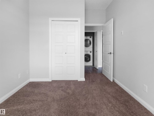 Plush carpeting, bi-fold closet doors, and a laundry area with stacked appliances and wood-finish flooring - #415 2588 Anderson Wy Sw, Edmonton, AB 