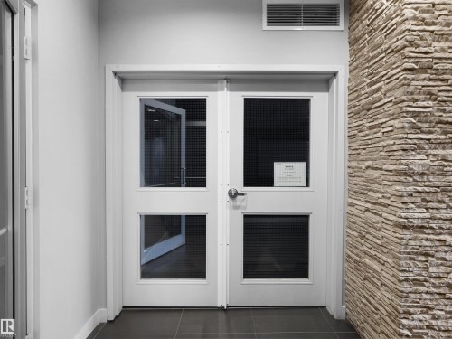 Double doors with glass inserts, stone accent wall, and dark tile flooring - #415 2588 Anderson Wy Sw, Edmonton, AB 