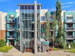 Modern multi-story building featuring a glass and metal facade, stone accents, multiple private balconies, and a prominent glass-enclosed stairwell - 