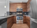 Kitchen featuring wood-finish cabinetry, stainless steel appliances, dark subway tile backsplash, light-toned countertops, and wood-finish flooring - #415 2588 Anderson Wy Sw, Edmonton, AB 