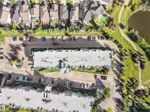 Aerial perspective showcasing a multi-unit residential building, adjacent paved parking areas, and a nearby natural area with a water feature - #415 2588 Anderson Wy Sw, Edmonton, AB 