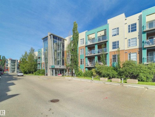 Modern multi-story building featuring a prominent glass and stone-clad entrance - #415 2588 Anderson Wy Sw, Edmonton, AB 