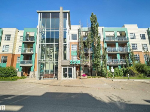 Modern multi-story building featuring a prominent glass-enclosed entrance, exterior balconies, and a vibrant multi-color facade - #415 2588 Anderson Wy Sw, Edmonton, AB 
