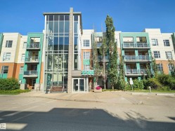 Modern multi-story building featuring a prominent glass-enclosed entrance, exterior balconies, and a vibrant multi-color facade - 