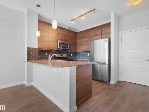 Kitchen featuring wood-finish cabinetry, stainless steel appliances, granite-look countertops, subway tile backsplash, and wood-finish flooring - #415 2588 Anderson Wy Sw, Edmonton, AB 