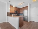 Kitchen featuring wood-finish cabinetry, stainless steel appliances, granite-look countertops, subway tile backsplash, and wood-finish flooring - #415 2588 Anderson Wy Sw, Edmonton, AB 