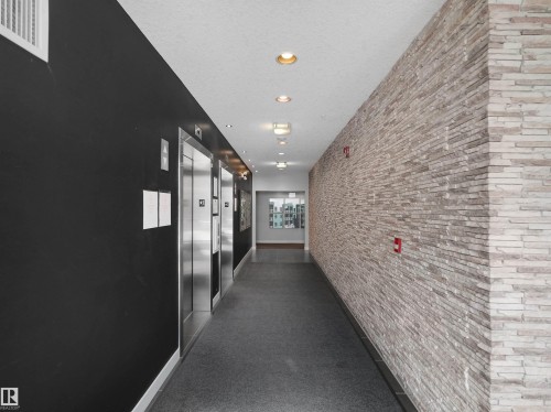 Hallway featuring textured stone veneer wall, recessed lighting, and stainless steel elevator doors - #415 2588 Anderson Wy Sw, Edmonton, AB 