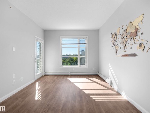 Wood-finish flooring throughout, white painted walls, and a large window with horizontal blinds - #415 2588 Anderson Wy Sw, Edmonton, AB 