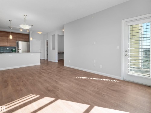Open-concept living space featuring wood-finish flooring, a kitchen island with pendant lighting, stainless steel appliances, and a glass-paned door to the exterior - #415 2588 Anderson Wy Sw, Edmonton, AB 