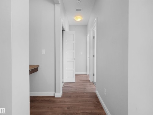 Hallway with wood-finish flooring, white paneled doors, and a built-in floating desk - #415 2588 Anderson Wy Sw, Edmonton, AB 