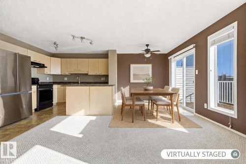 Kitchen area featuring light-toned cabinetry, stainless steel refrigerator, dark-toned countertop, and track lighting, with sliding glass door access to an exterior balcony - 9047 Scott Crescent Nw, Edmonton, AB 