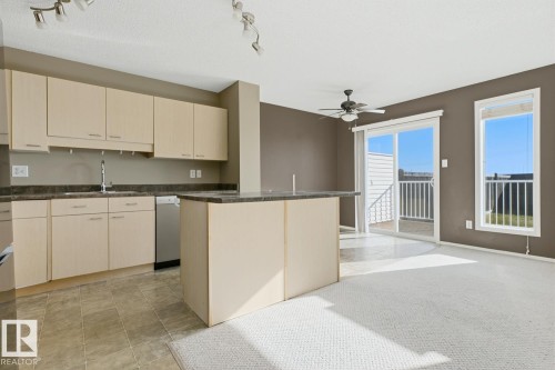 Kitchen featuring light-finish cabinetry, a central island, stainless steel dishwasher, tile flooring, and sliding glass doors to exterior space - 9047 Scott Crescent Nw, Edmonton, AB 
