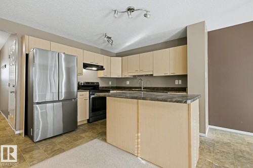 Kitchen featuring light-tone cabinetry, a central island with stone-finish countertop, stainless steel refrigerator, black range, and tile flooring - 9047 Scott Crescent Nw, Edmonton, AB 