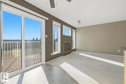Room featuring large sliding glass doors, built-in fireplace with stone-finish surround, vertical windows, neutral carpeting, and a ceiling fan - 9047 Scott Crescent Nw, Edmonton, AB 