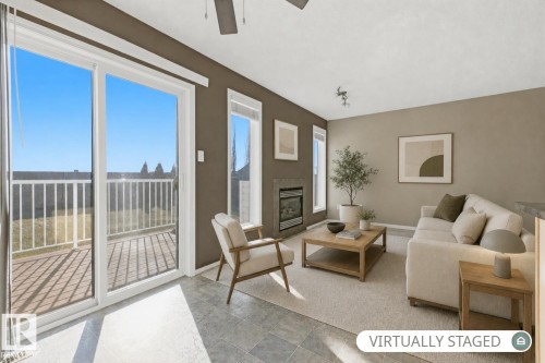 Bright corner living space with expansive glass doors and windows offering natural light, wood-finish flooring, neutral wall finishes, and a fireplace with surround - 9047 Scott Crescent Nw, Edmonton, AB 