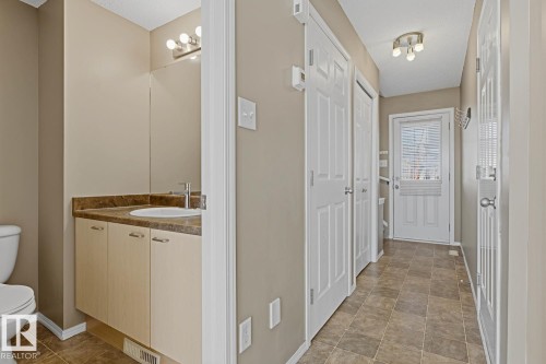 Bathroom featuring a vanity with light wood-finish cabinetry, a stone-composite countertop, and an integrated basin, finished with tile flooring and a multi-panel door entry - 9047 Scott Crescent Nw, Edmonton, AB 