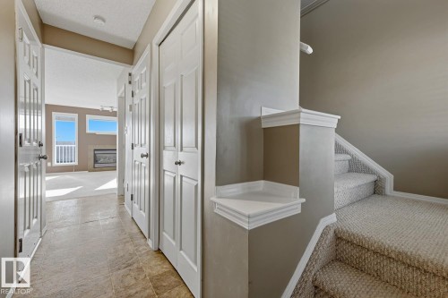 Entryway featuring tiled flooring, carpeted stairs with a white millwork half-wall, dual bi-fold closet doors, and a paneled entry door - 9047 Scott Crescent Nw, Edmonton, AB 