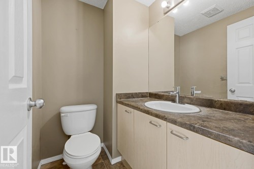 Vanity featuring light-tone cabinetry, a dark-toned solid surface countertop, and an integrated oval sink with a chrome faucet, accompanied by a full-width wall mirror and a three-light fixture - 9047 Scott Crescent Nw, Edmonton, AB 