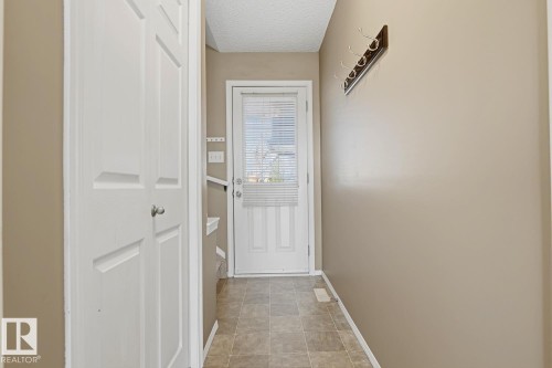 Entryway featuring stone-tile flooring, a paneled door with integrated glass, and a wall-mounted hook rack - 9047 Scott Crescent Nw, Edmonton, AB 