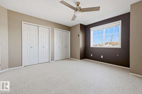 Room featuring neutral-toned walls, carpeting, dual bi-fold closets, a multi-pane window, and a ceiling fan with integrated lighting - 9047 Scott Crescent Nw, Edmonton, AB 