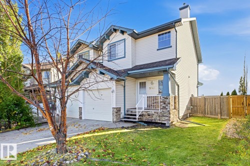 Two-story exterior featuring light-colored siding, a stone veneer foundation, dual garage doors, and a covered front porch with white railing - 9047 Scott Crescent Nw, Edmonton, AB 