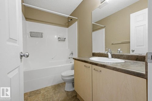 Bathroom featuring a vanity with wood-finish cabinetry, an oval drop-in sink, a full-width wall mirror, and a tub-shower combination with a surround - 9047 Scott Crescent Nw, Edmonton, AB 