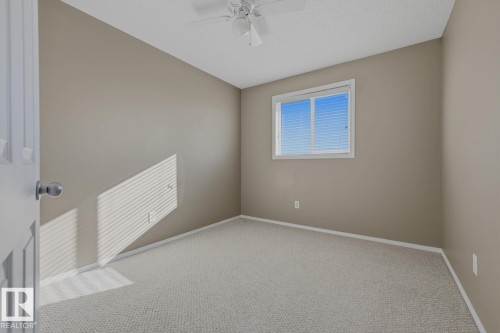 Neutral-toned interior space featuring wall-to-wall carpeting, a ceiling fan with integrated lighting, and a single sliding window - 9047 Scott Crescent Nw, Edmonton, AB 