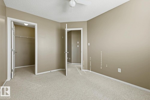 Neutral-toned room featuring neutral carpeting, textured ceiling, ceiling fan with light fixture, and a built-in walk-in closet with shelving - 9047 Scott Crescent Nw, Edmonton, AB 