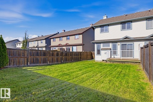 Rear yard featuring a manicured lawn, wood fencing, and a raised wooden deck with white railing - 9047 Scott Crescent Nw, Edmonton, AB 