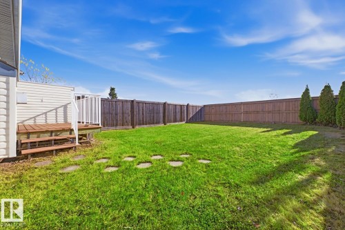Fenced-in backyard featuring a wood-plank deck, stone paver path, manicured lawn, and mature perimeter trees - 9047 Scott Crescent Nw, Edmonton, AB 