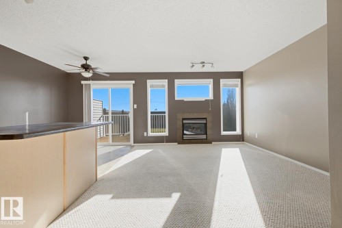 Living area featuring carpeted flooring, a fireplace with a stone-finish surround, a ceiling fan, and sliding glass doors - 9047 Scott Crescent Nw, Edmonton, AB 