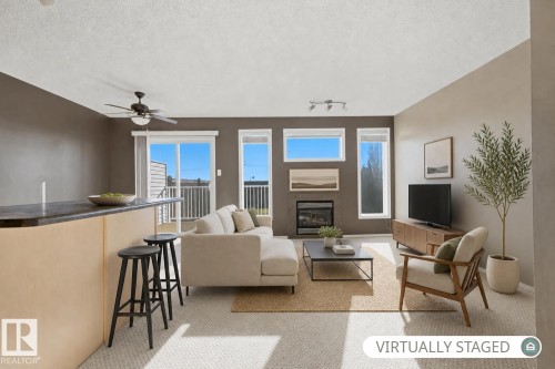 Living area featuring a fireplace with a horizontal window above, ceiling fan, track lighting, and sliding glass door with access to an exterior balcony - 9047 Scott Crescent Nw, Edmonton, AB 