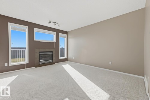 Living space featuring a tiled fireplace, three vertical and horizontal windows, neutral wall colors, and carpeting - 9047 Scott Crescent Nw, Edmonton, AB 