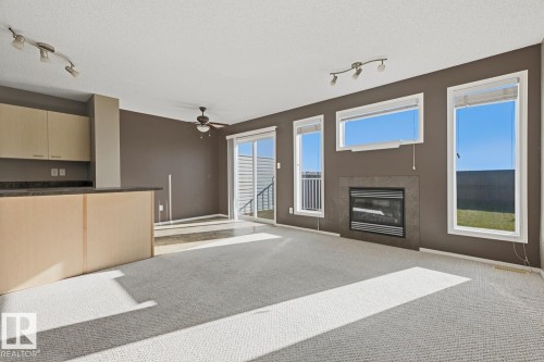 Living area featuring a fireplace with stone-finish surround, sliding glass door, multi-panel windows, built-in cabinetry, and integrated track lighting - 9047 Scott Crescent Nw, Edmonton, AB 
