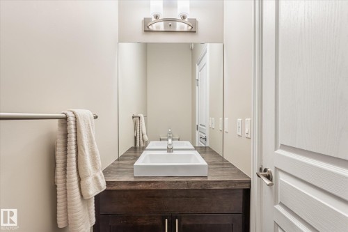 Wood-finish vanity with dual vessel sinks, full-width mirror, and wall-mounted light fixture - 21935 91 Avenue Nw, Edmonton, AB 