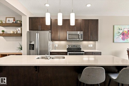 Kitchen island with undermount sink, pendant lighting, stainless steel appliances, dark wood-finish cabinetry, and light-toned countertops - 21935 91 Avenue Nw, Edmonton, AB 