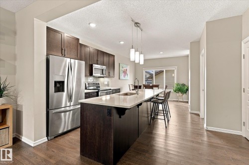 Kitchen featuring stainless steel appliances, dark wood-finish cabinetry, a large center island with a sink, pendant lighting, and wood-finish flooring - 21935 91 Avenue Nw, Edmonton, AB 