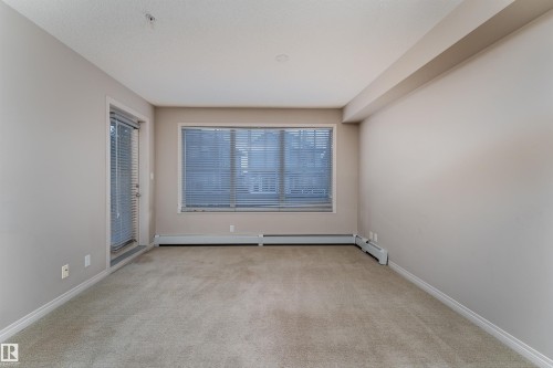 Neutral carpeting throughout, featuring a large window with blinds, a glass-paneled door with blinds, and perimeter baseboard heating - #202 105 Ambleside Dr Sw, Edmonton, AB 