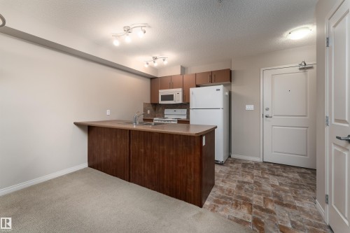 Kitchenette featuring wood-finish cabinetry, white appliances, and a breakfast bar - #202 105 Ambleside Dr Sw, Edmonton, AB 