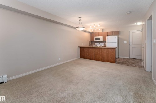 Open-concept living area featuring a kitchen with wood-finish cabinetry, white appliances, and a breakfast bar - #202 105 Ambleside Dr Sw, Edmonton, AB 
