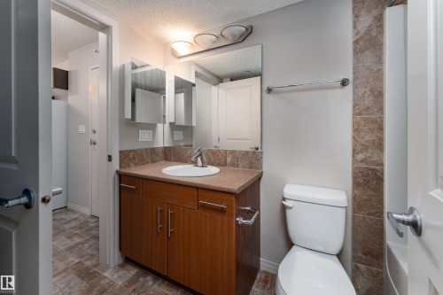 Bathroom featuring a wood-finish vanity with an integrated sink, polished chrome faucet, and a large mirror - #202 105 Ambleside Dr Sw, Edmonton, AB 