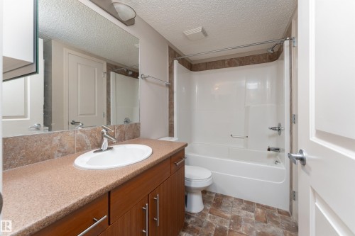 Bathroom featuring a wood-finish vanity with a single basin sink, a tiled backsplash, and a combination bathtub and shower with a tiled surround - #202 105 Ambleside Dr Sw, Edmonton, AB 