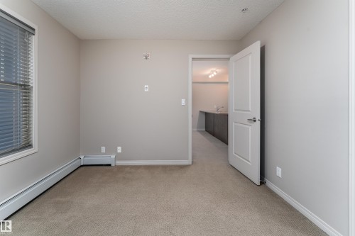 Textured carpeted flooring, neutral wall paint, and window with horizontal blinds - #202 105 Ambleside Dr Sw, Edmonton, AB 